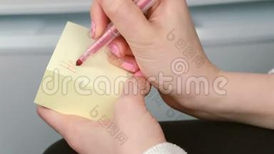 特写女人`她的手写在黄色的贴纸纸上，字玩得很开心。